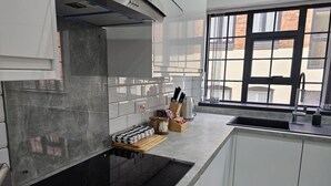 Une cuisine moderne avec une plaque de cuisson noire, des placards blancs et une fenêtre équipée de stores.