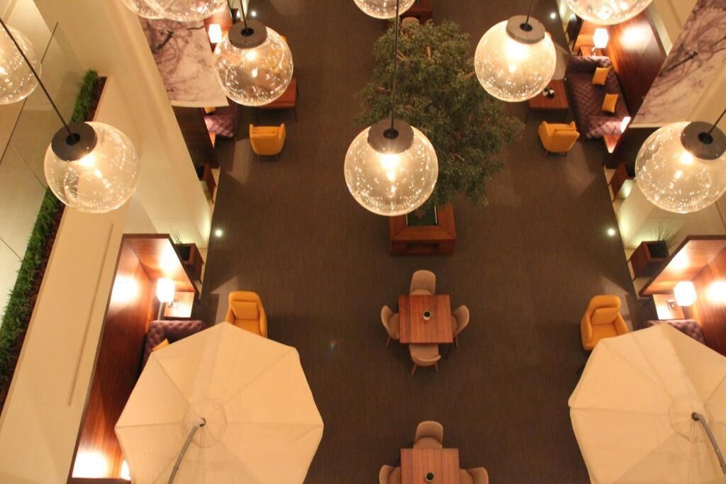 A hotel lobby with multiple seating areas, including round tables and chairs, and large umbrellas.