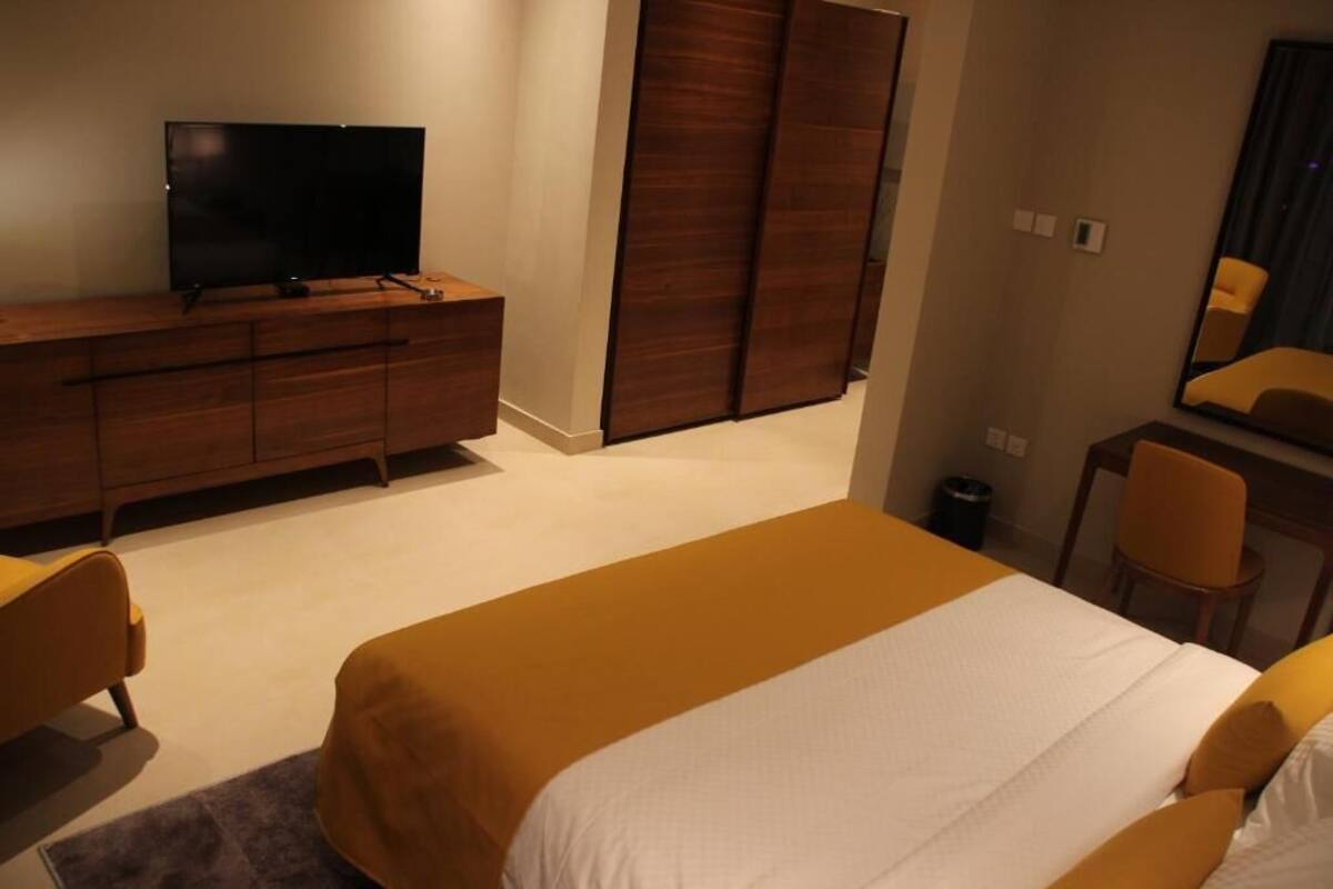 A hotel room with a bed, a television on a wooden dresser, a mirror, and a chair.