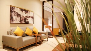 Ein modernes Wohnzimmer mit Sofa, Sesseln und Couchtisch. Ein großes abstraktes Gemälde hängt an der Wand, und im Vordergrund steht eine Pflanze.