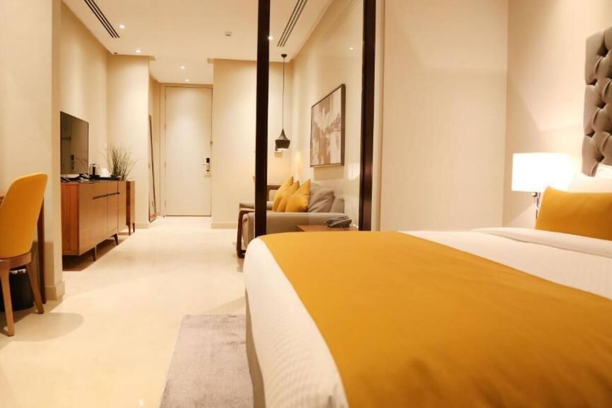 A hotel room with a large bed, a desk with a chair, a sofa, and a television.