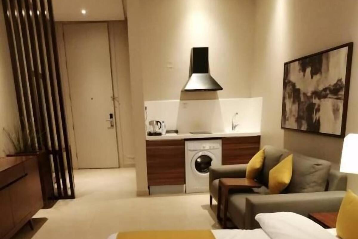 A modern hotel room with a large bed, a sofa, a coffee table, and a small kitchenette.