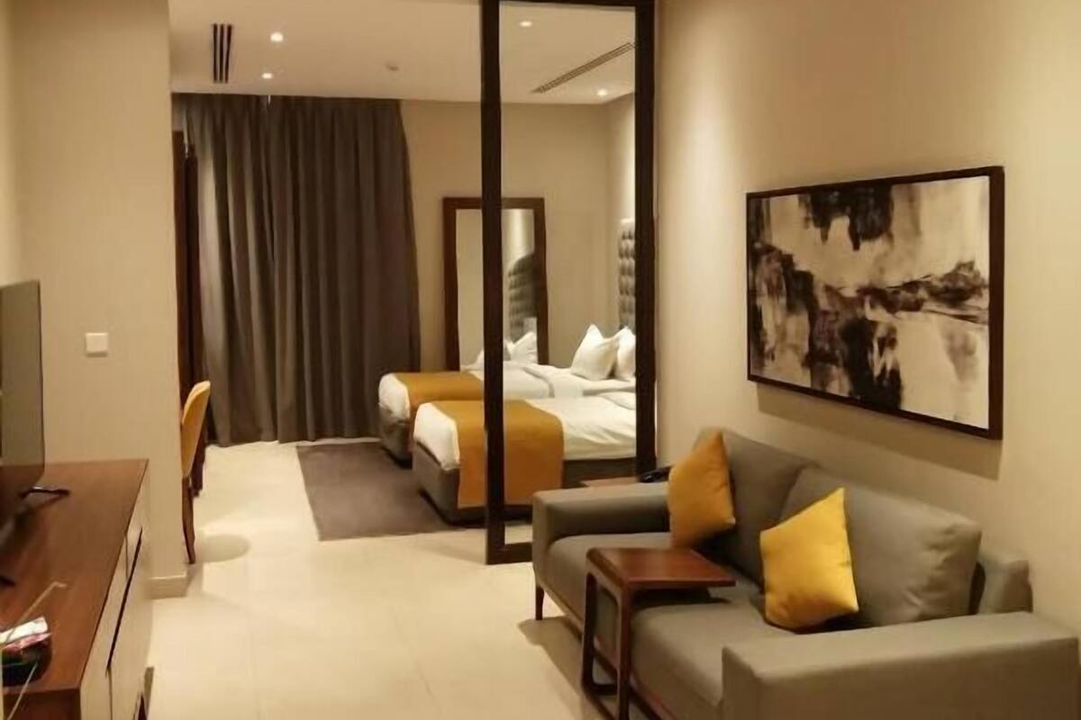 A modern hotel room with a sofa, a bed, a desk, and a large mirror.