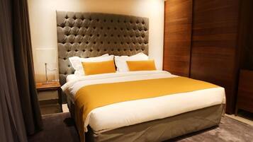 Une chambre d’hôtel avec une tête de lit capitonnée, un lit avec une literie blanche et moutarde, et une armoire en bois.