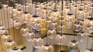 Eine großzügige Lobby mit mehreren Sitzbereichen, hängenden, kugelförmigen Leuchten und künstlichen Bäumen.