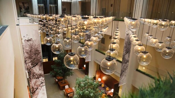 Eine Hotelhalle mit mehreren Etagen, hängenden Kugelleuchten, Zimmerpflanzen und Sitzbereichen.