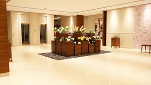 Eine Lobby mit zentralem Blumenarrangement, Holzbürorezeption und einer Wand mit Muster.