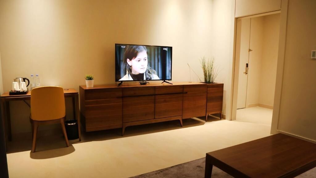 En stue med et fjernsyn på et træskab, en sofa, et sofabord og en lille plante.