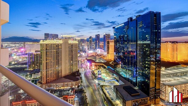 Un hotel de gran altura con varios pisos, una fachada de vidrio destacada y vistas a un paisaje urbano con edificios e iluminaciones en las calles.