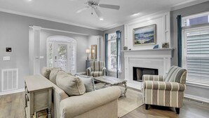 A living room with a sofa, armchairs, a coffee table, a fireplace, and a ceiling fan. - Award-Winning Resort Amenities | Grand Pavilion 71 by Wild Dunes (Isle of Palms)