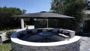 A circular stone fire pit with a table and chairs underneath a large umbrella. - La Villa de Jade (Orange)