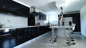 A modern kitchen with black cabinets, a white countertop, and a central island with bar stools. - La Villa de Jade (Orange)