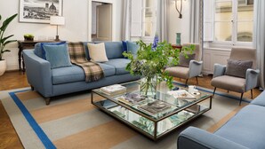A spacious living room with a blue sofa, a glass coffee table, and a large window with curtains. - Conte Jacopo - La Dimora degli Affreschi Florence (Florence)