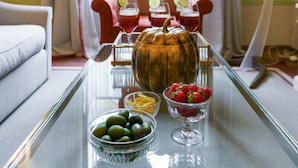 Une table à plateau en verre sur laquelle on trouve une citrouille, un bol d’olives vertes, un bol de fraises et deux verres contenant une boisson rouge.