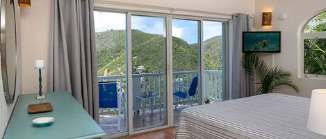 Une chambre à coucher comprenant un lit, un bureau, une chaise, un téléviseur et un balcon avec vue sur les collines.