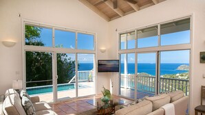 A spacious living room with large windows offering ocean views, a comfortable sofa, a coffee table, and a TV. - Sea Turtle Villa: Stunning Views! Newly Refurnished! (St John)