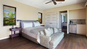 Un dormitorio con una cama grande, un escritorio, un ventilador de techo y vistas al exterior a través de la ventana.
