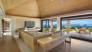 Una sala moderna con un sofá grande, una mesa de centro y un televisor montado en la pared. Hay un ventanal con vistas al océano.