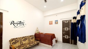 A reception area with a sofa, a table with a red patterned tablecloth, and a door with curtains. - Swastik Hotel  (Deoghar)