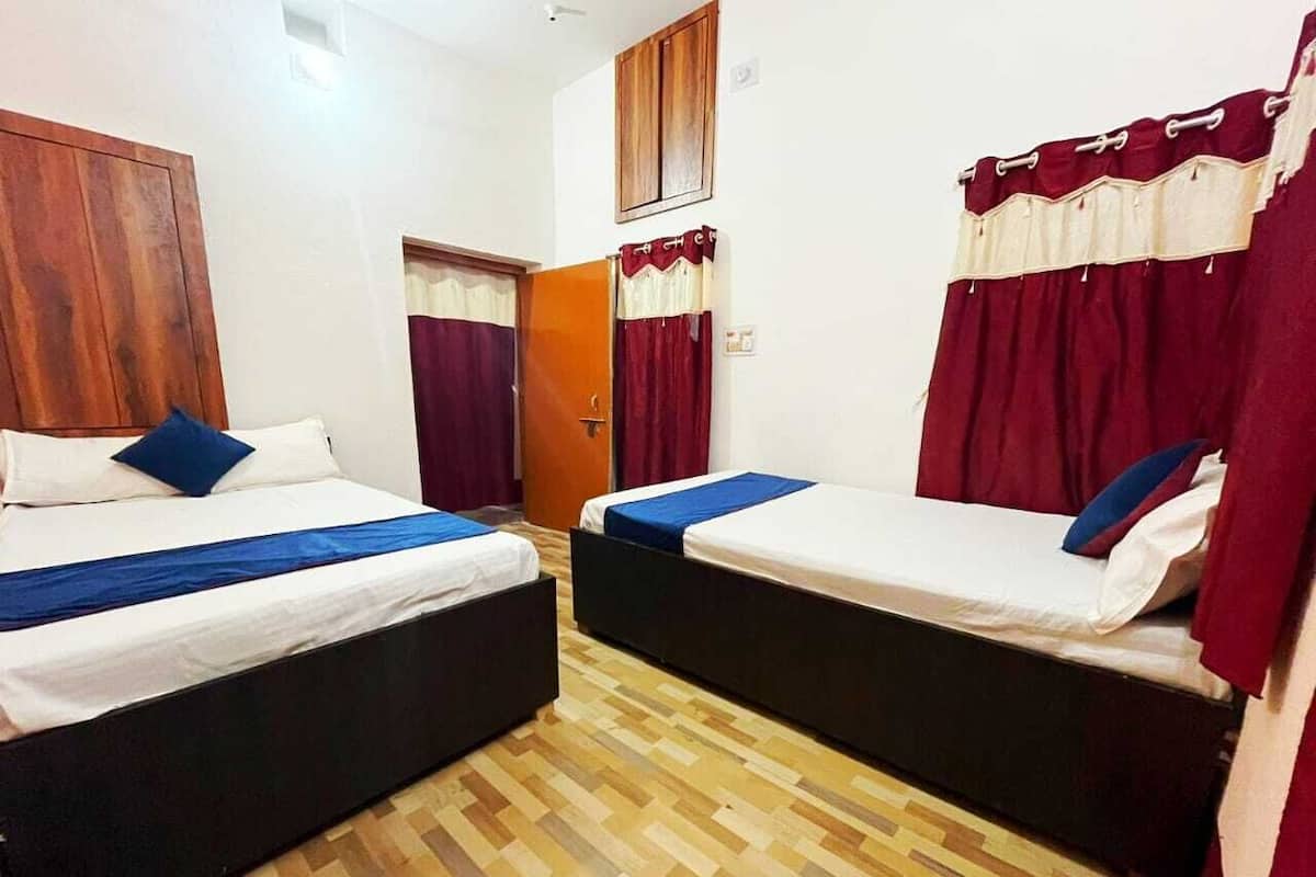 A room with two single beds, wooden flooring, and red curtains.