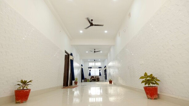 A spacious hallway with white brick walls, two ceiling fans, and potted plants on either side. - Swastik Hotel  (Deoghar)