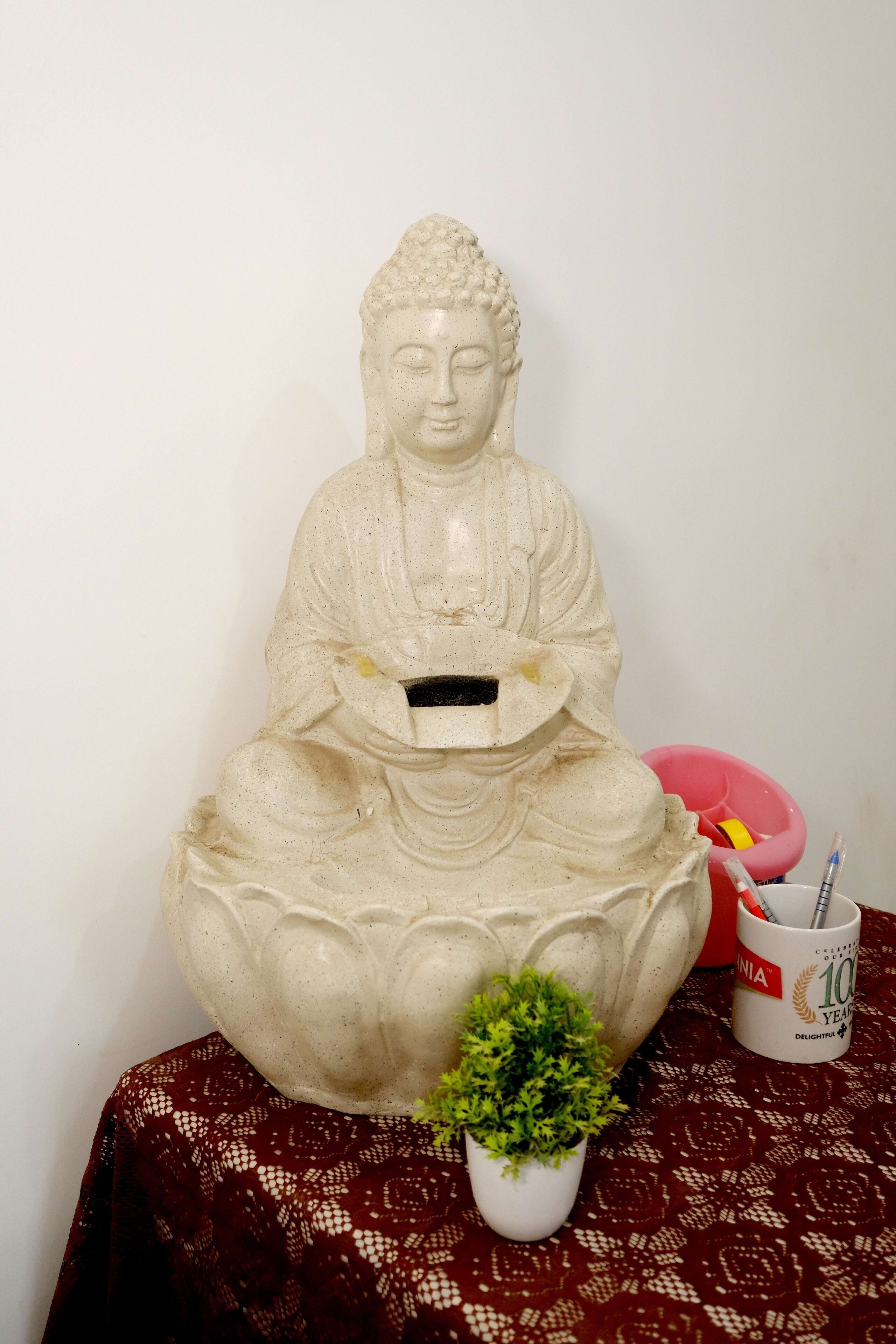 A statue of a seated figure with a bowl in its hands, placed on a patterned tablecloth.
