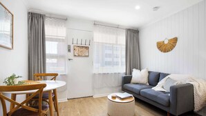 Ein Wohnzimmer mit grauem Sofa, Holzstühlen, einem runden Hocker und einem Esstisch.