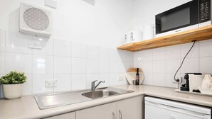 Eine Küche mit Spülbecken aus Edelstahl, einer Mikrowelle, einem Holzregal, einem Geschirrspüler und einem Blumentopf.