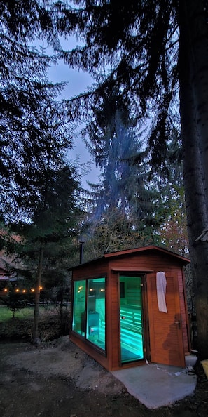 A small wooden cabin with a glass door and windows, surrounded by trees.