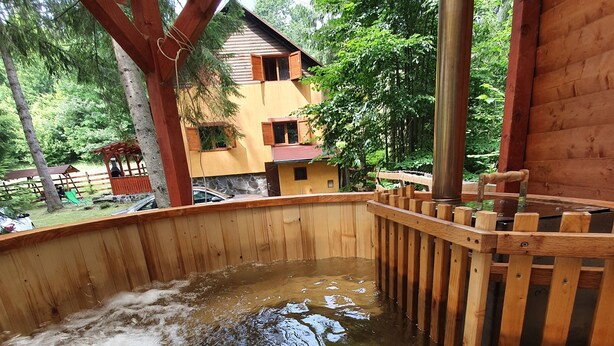 A wooden hot tub with a wooden deck and metal railing, surrounded by a wooden pergola and a stone wall. - Private vacation home in the middle of the Harghita mountains surrounded by (Vărșag)