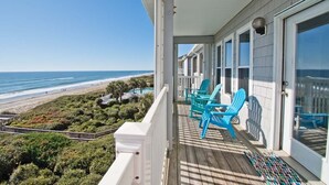 Ein Balkon mit Blick auf den Strand, einer Holzterrasse und blauen Stühlen.