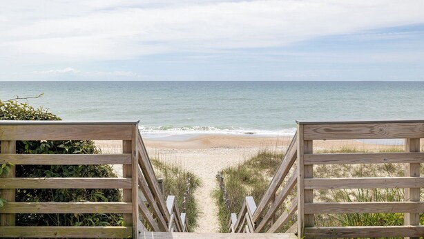 Una escalera de madera que lleva a una playa con vista al océano.