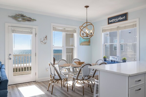 A coastal dining area with wicker chairs, a glass table, and a view of the ocean through large windows.