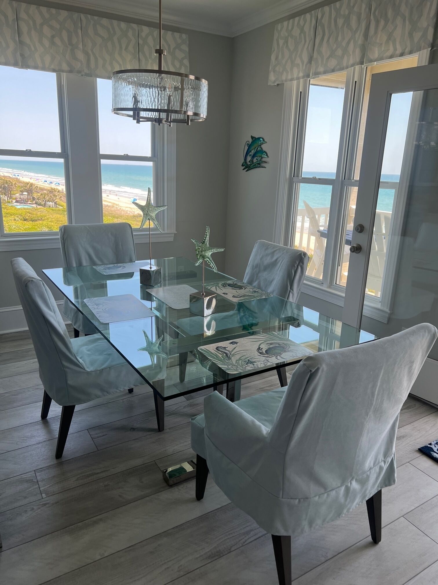 Un coin repas avec une table en verre et des chaises blanches, donnant sur une plage.