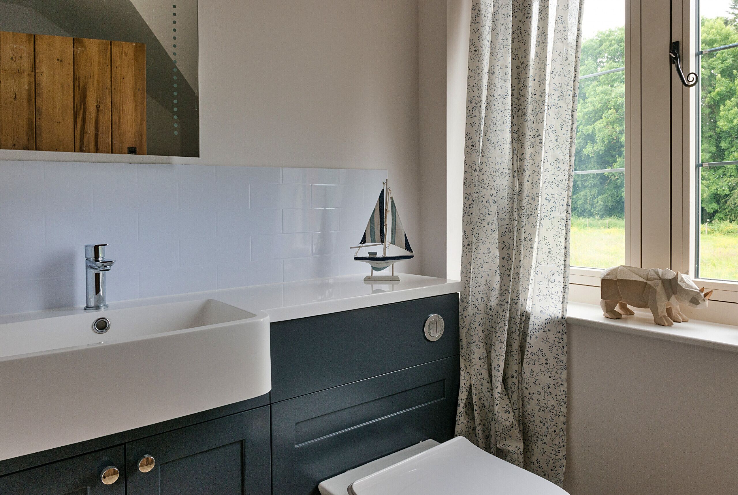 A bathroom with a white sink, dark cabinet, and a window with a view of greenery.