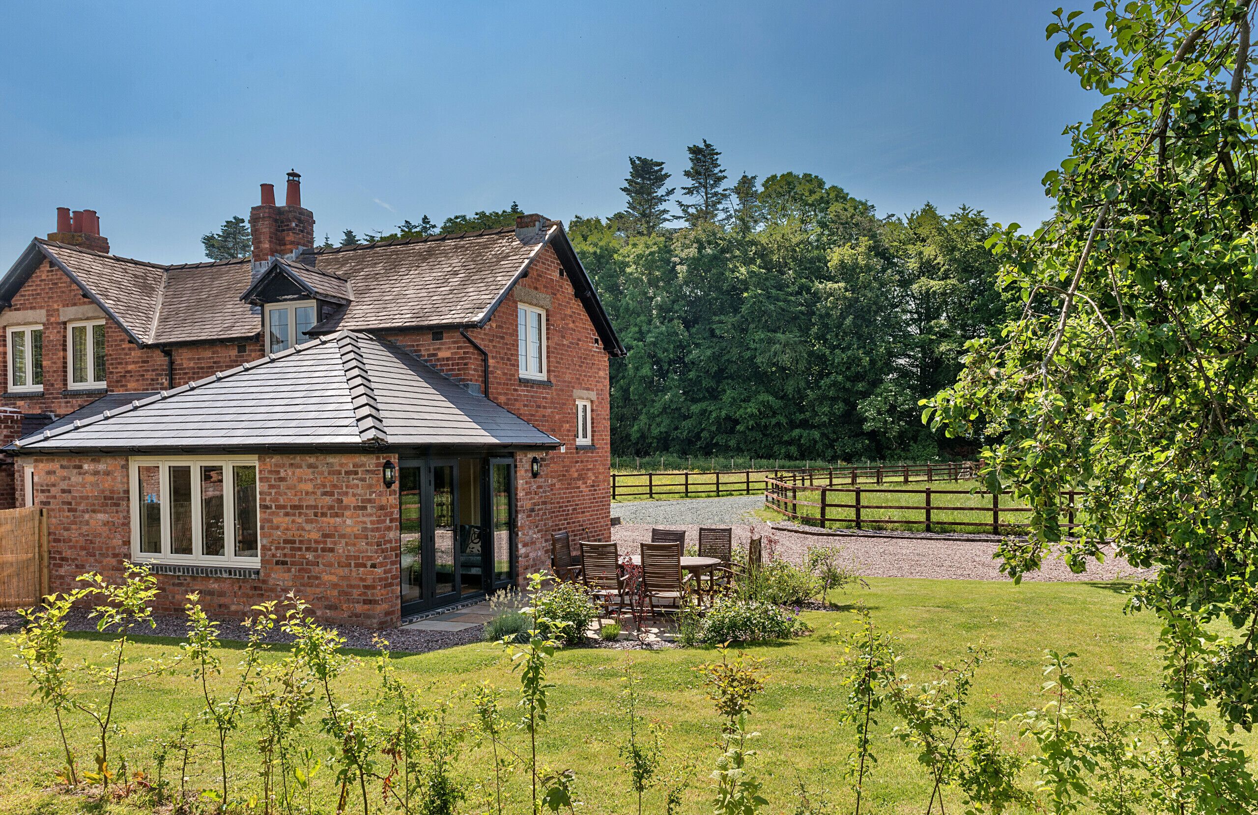 A brick house with a sloped roof, a patio with outdoor furniture, and a fenced yard.