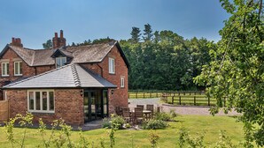A brick house with a sloped roof, a patio with outdoor furniture, and a fenced yard. - Fox and Hare (Shrawardine)