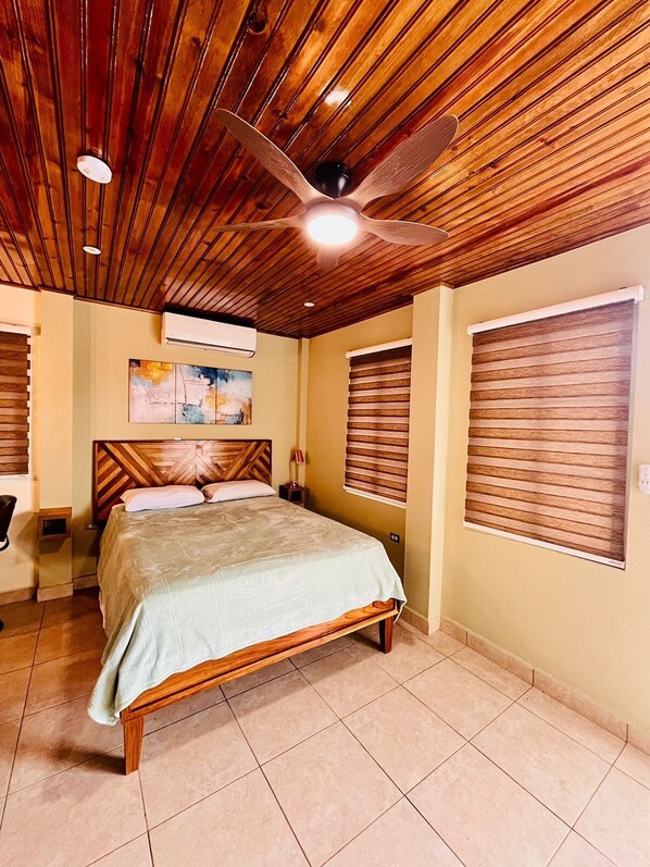 Un dormitorio con techo de madera, una cama, ventilador de techo y ventana con persianas.