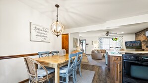 Ein Essbereich mit Holztisch und Stühlen, einer Deckenleuchte sowie eine Küche mit Herd und Backofen.