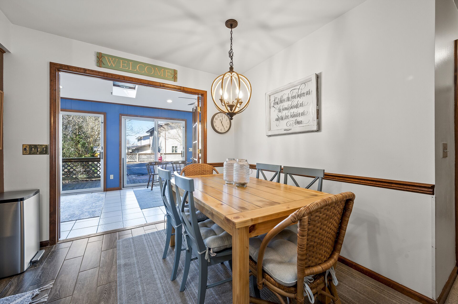 Un'area pranzo con un tavolo in legno e sedie in vimini, un lampadario e una sveglia appesa al muro.