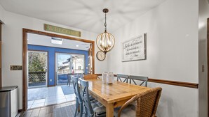 Ein Essbereich mit Holztisch, Korbstühlen, einer Chandelüster und einer Wanduhr.