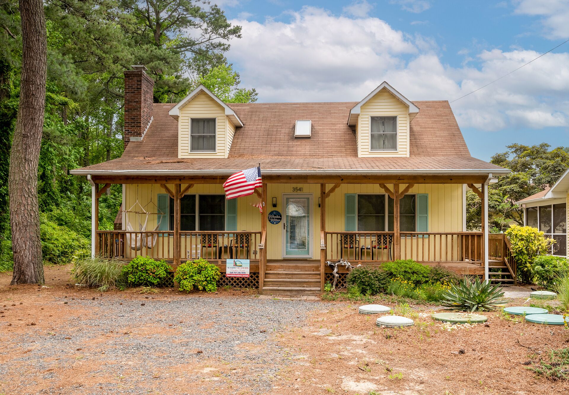 A two-story house with a porch, a small attached garage, and a front yard with a gravel path and potted plants.