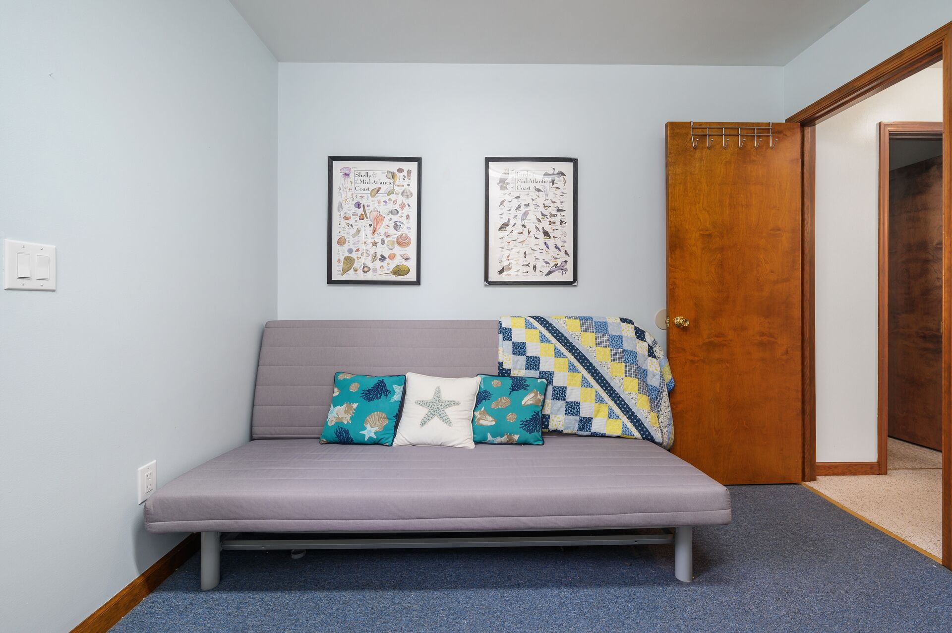 A small, modern room with a grey sofa, two framed coastal-themed wall art pieces, and a wooden door.