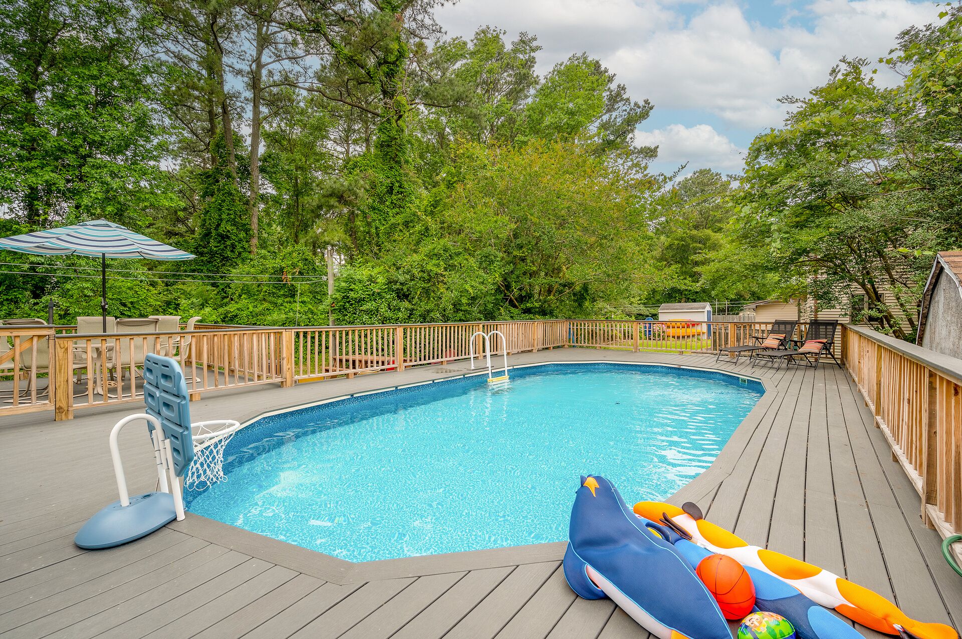 A swimming pool with a wooden deck, surrounded by trees.