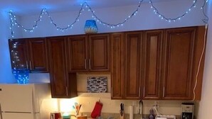 A kitchen with wooden cabinets, a refrigerator, a stove, and a dining area with a table set for two. - Beach Side Hideaway 1 Bedroom Condo by RedAwning (Norfolk)