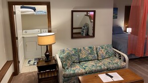 A hotel room with a sofa, a small table with a remote control, a mirror, and a bed with a canopy. - Beach Side Hideaway 1 Bedroom Condo by RedAwning (Norfolk)