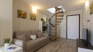 Een moderne woonkamer met een bank, een salontafel, een televisie, een trap en kunstwerken aan de muur.