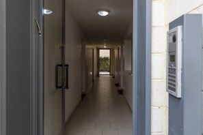 A corridor with a tiled floor, a glass door on the left, and a utility box on the right. - notami - Salomone - Mecenate District (Milan)