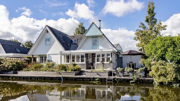 A traditional house with a gabled roof, a covered porch, and a reflection in the water in front.