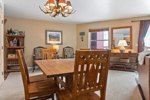 A dining room with a wooden table and chairs, a chandelier, a bookshelf, and a mirror.